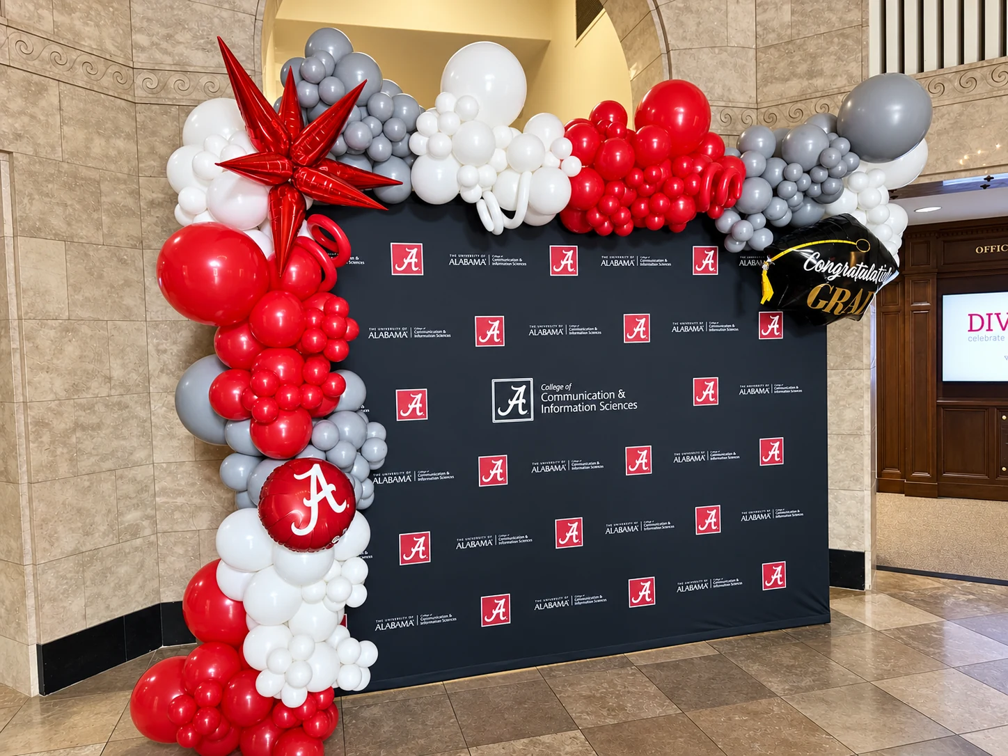 Crimson, white and silver branded balloon garland beside a university backdrop