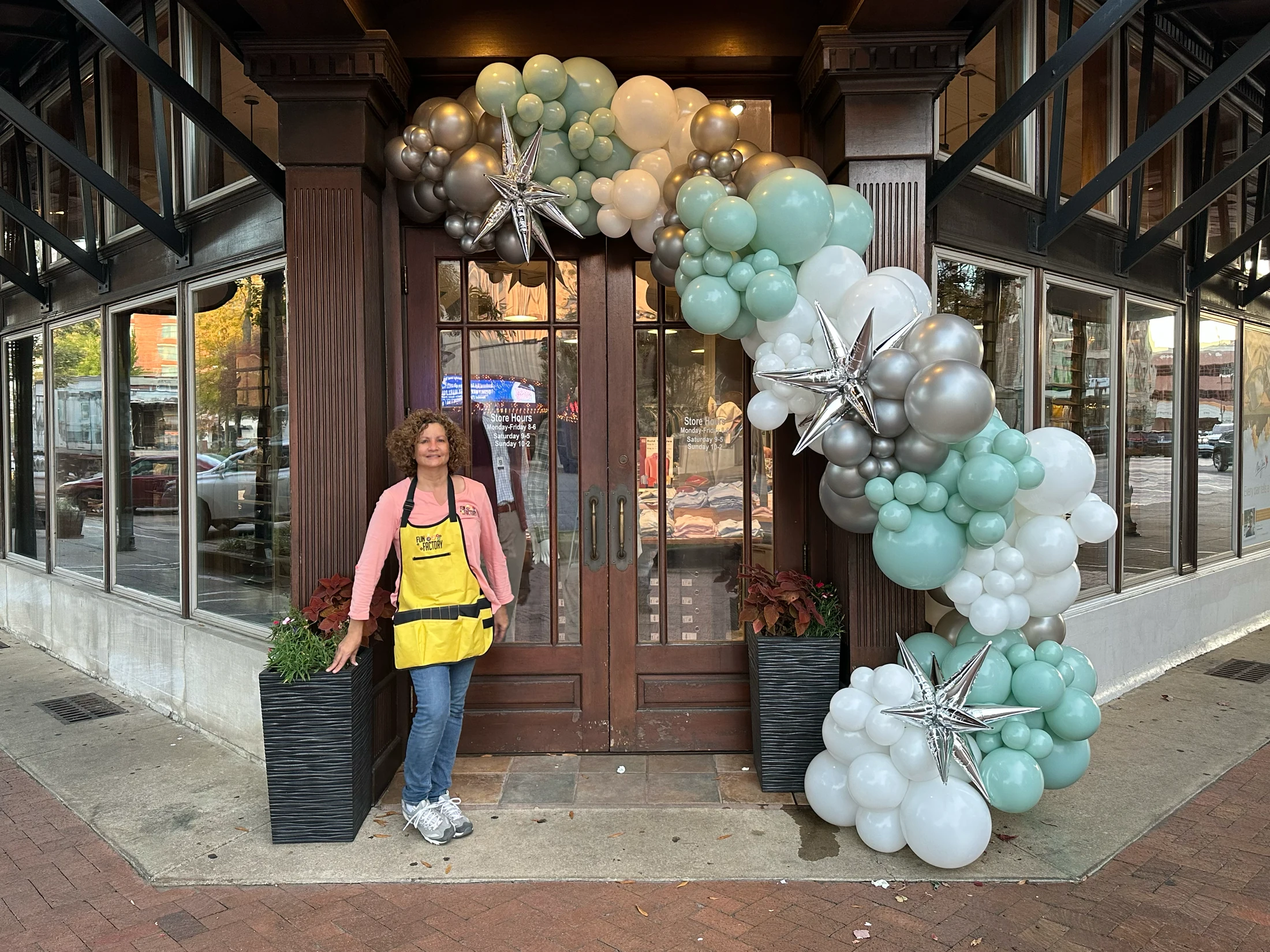 Artistic Balloon Co designer beside a mint, white and silver storefront balloon garland