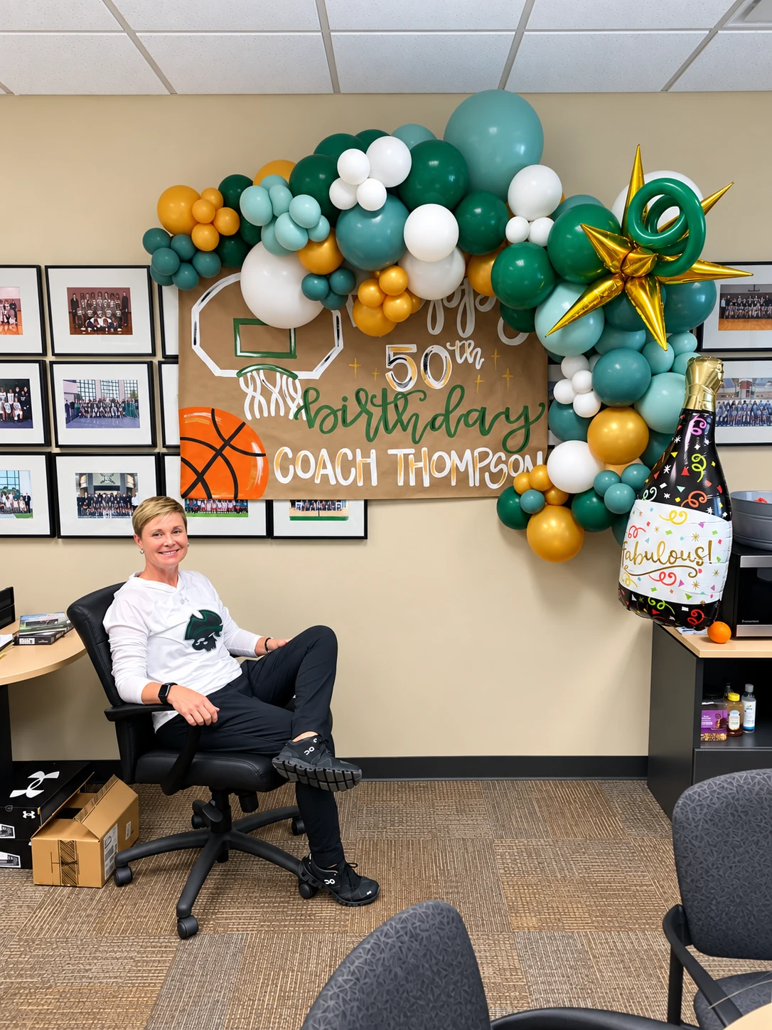 Green, white and gold coach birthday balloon garland in an office