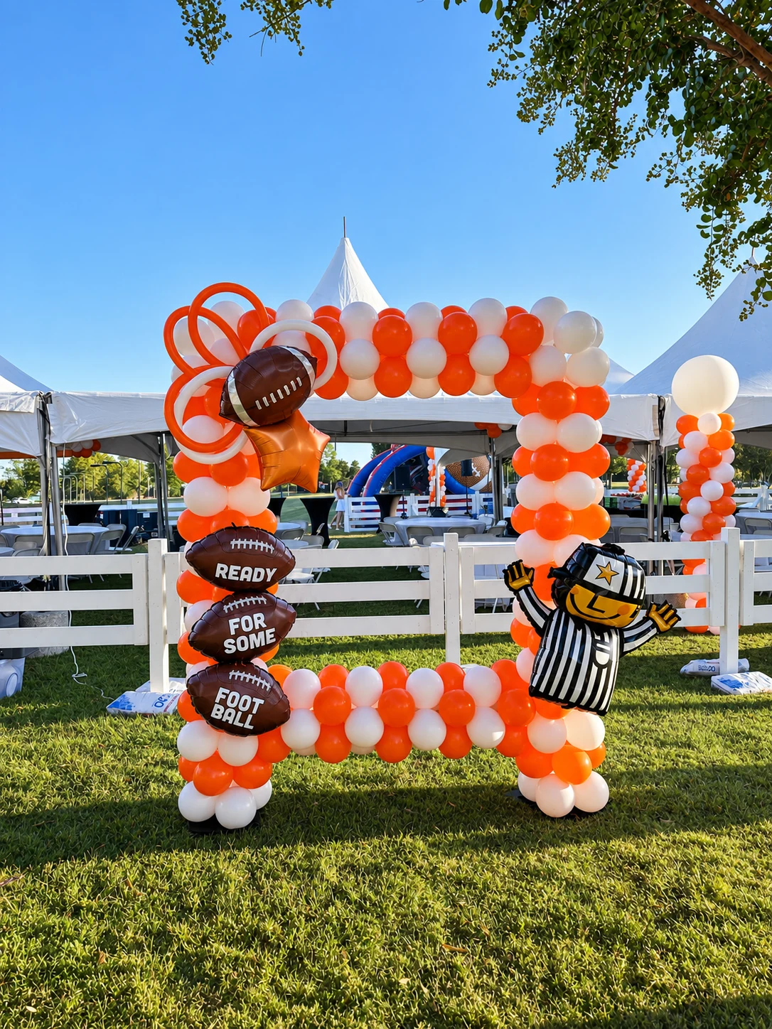 Orange and white football-themed balloon photo frame at an outdoor event