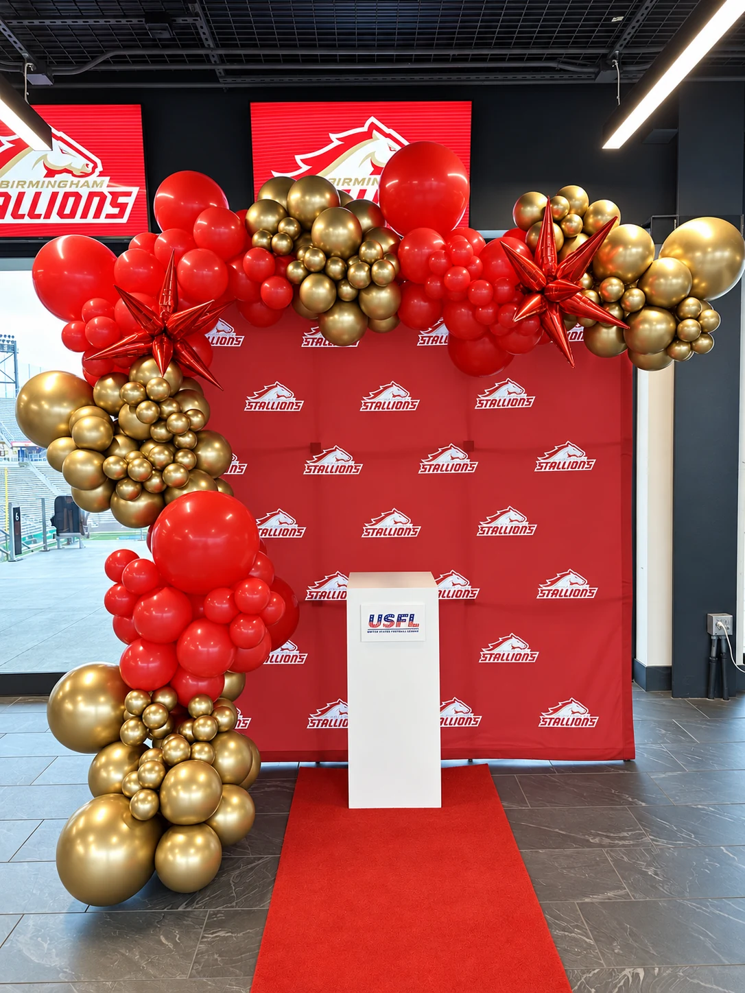 Red and gold organic balloon garland framing a branded event backdrop